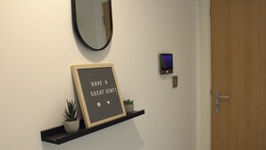 Un estante montado en la pared con un letrero motivacional, una pequeña planta en maceta y un termostato digital.