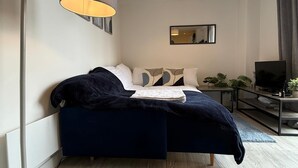 Un dormitorio moderno con una cama azul oscuro, una lámpara de pie, un televisor y un espejo en la pared.