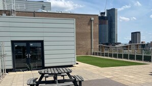Un edificio moderno con puerta de vidrio, una mesa de picnic y una zona pavimentada con césped.