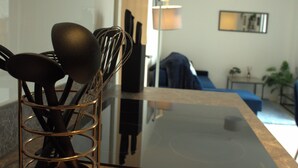 Una zona de cocina con encimera negra, un portalápices de metal y el reflejo de una persona al fondo.