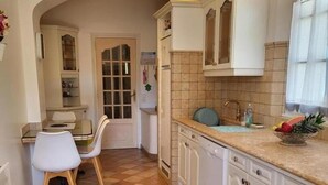 Una cucina con mobili bianchi, pavimento piastrellato e zona pranzo con tavolo e sedie.