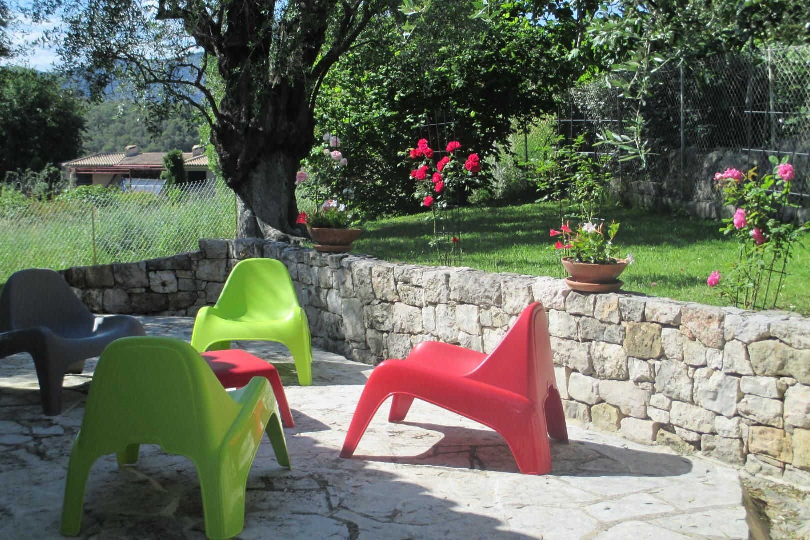 Un patio con muri in pietra e sedie di plastica colorate.