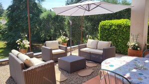 Un'area patio esterna con mobili in vimini, un tavolo con tovaglia floreale e un ombrellone.