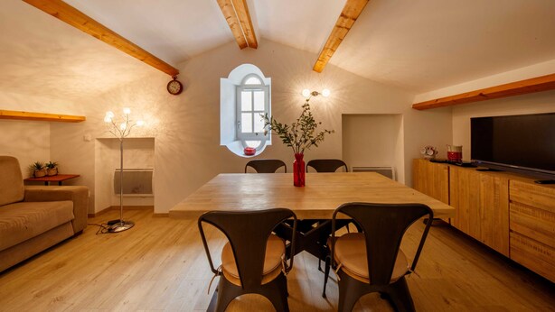 A cozy dining area with a wooden table, chairs, and a vase with flowers.