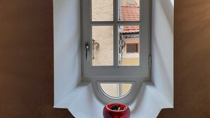 A room with a white arched window, a red bowl on the floor, and a view of a building with red tiles.