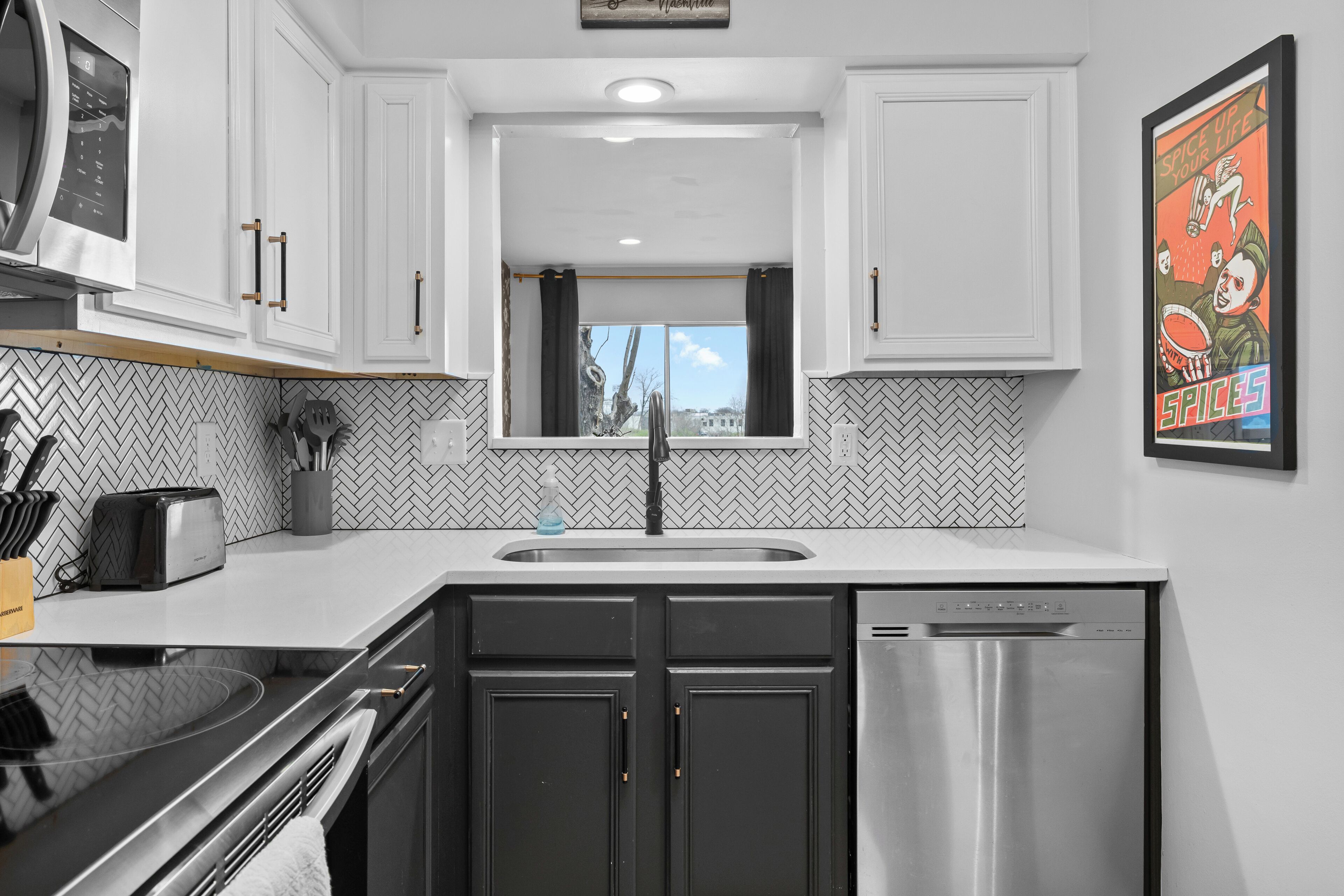 A modern kitchen with white cabinets, a stainless steel dishwasher, and a herringbone-patterned backsplash.