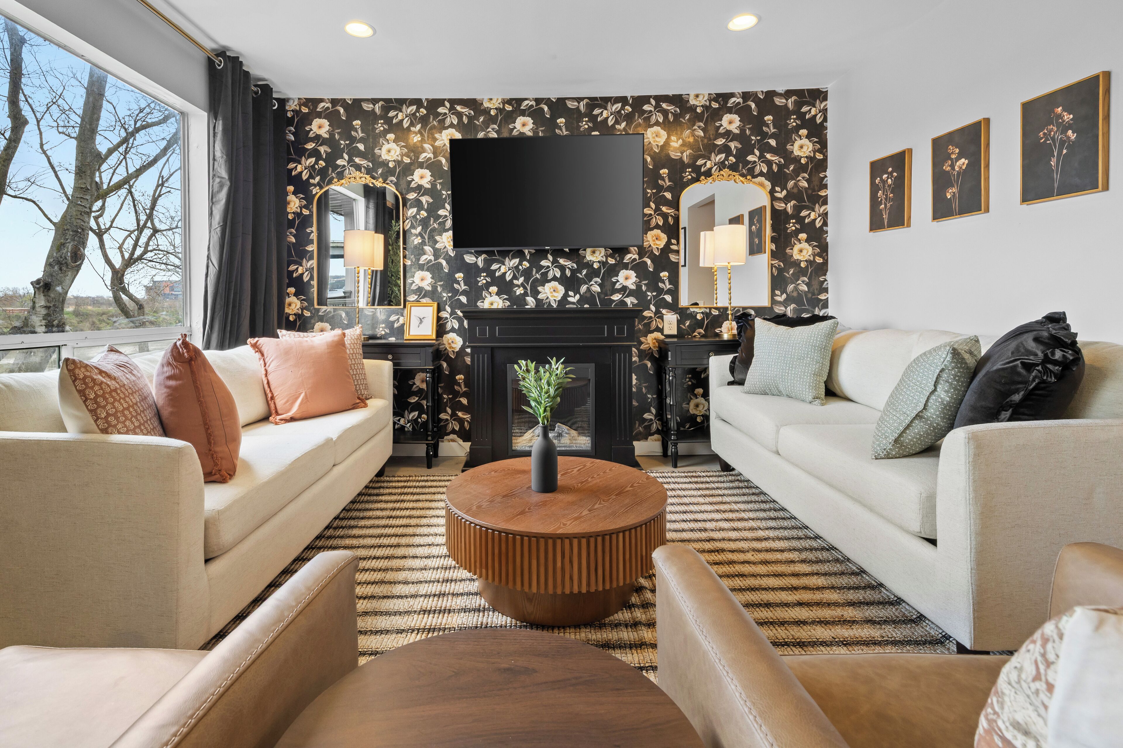 A living room with a sofa, armchair, round coffee table, fireplace, and a TV mounted on the wall.