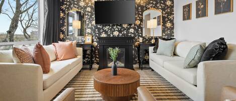 A living room with a sofa, armchair, round coffee table, fireplace, and a TV mounted on the wall.