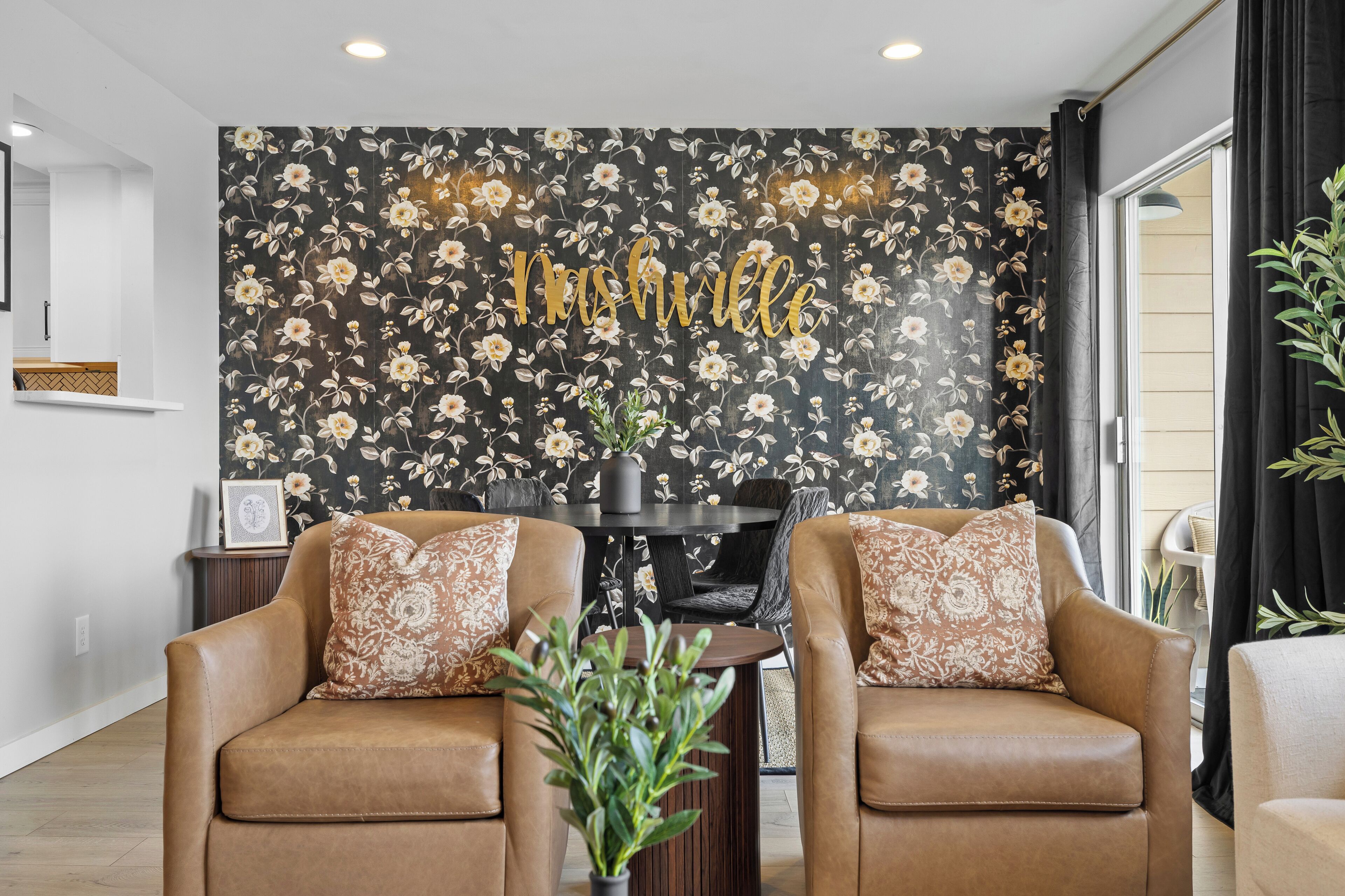 Un salon avec deux canapés en cuir marron, un papier peint à motifs floraux et une table ronde sur laquelle est posée une plante.