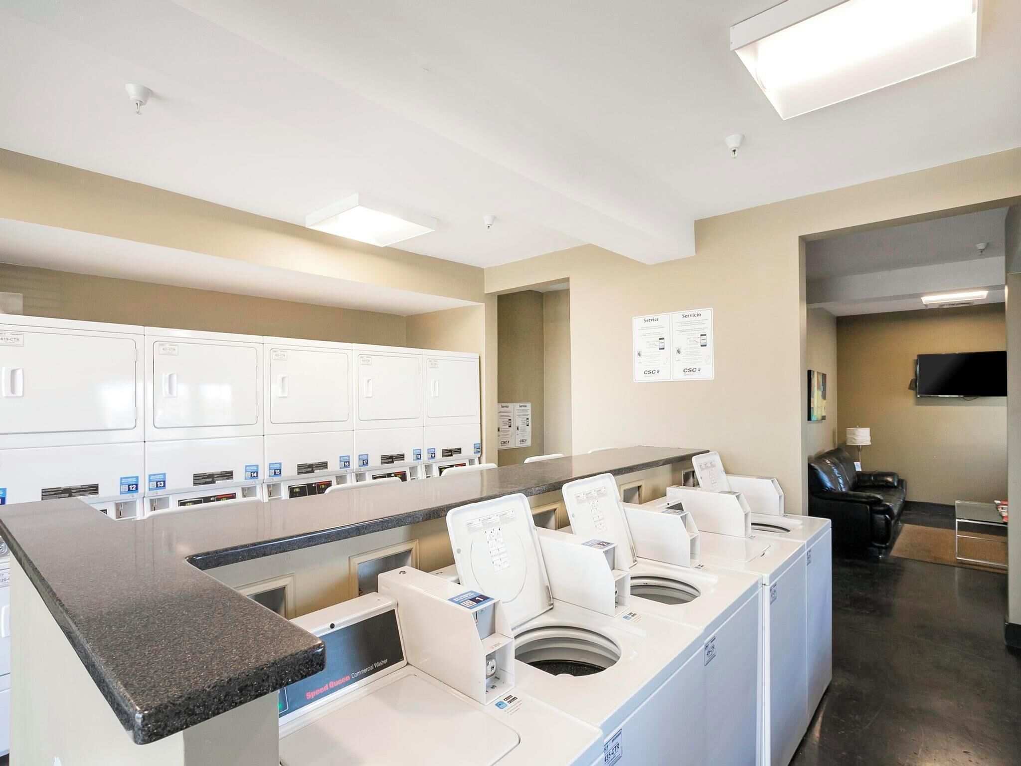 A hotel laundry room with multiple washing machines, a counter, and a seating area with a TV.