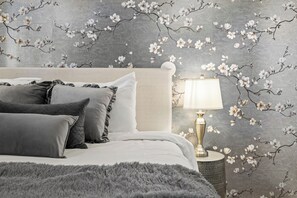 Quarto com cama, almofadas, tapete macio, mesa de cabeceira e abajur.