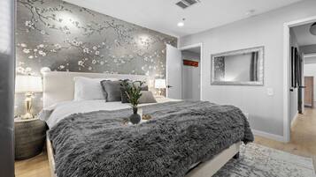 A bedroom with a bed, a nightstand, a lamp, a mirror, and a wall with a floral pattern.