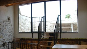 A room with a stone wall, a wooden table, a chair, a staircase with black railings, and a window with a view of the outside. - Le Ciste - SAINT-JEANNET (SAINT-JEANNET)