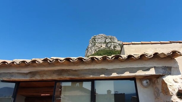 A building with a tiled roof, a stone structure on top, and a window with a view of the sky. - Le Ciste - SAINT-JEANNET (SAINT-JEANNET)