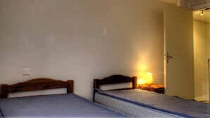 Una habitación con dos camas individuales, una lámpara de noche, una puerta y un interruptor de luz en la pared.