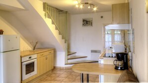 Cocina compacta con horno integrado, una mesa de comedor de madera, cafetera y una escalera con barandilla verde claro.