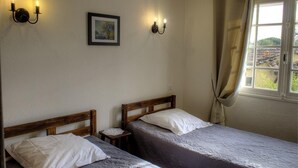 Une chambre avec deux lits en bois, une table de chevet, un tableau encadré au mur et une fenêtre avec des rideaux.
