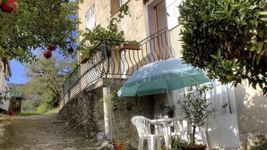 Un escalier en pierre mène à un bâtiment doté d’un balcon, d’un espace extérieur aménagé avec des chaises en plastique blanches et de plantes en pot.