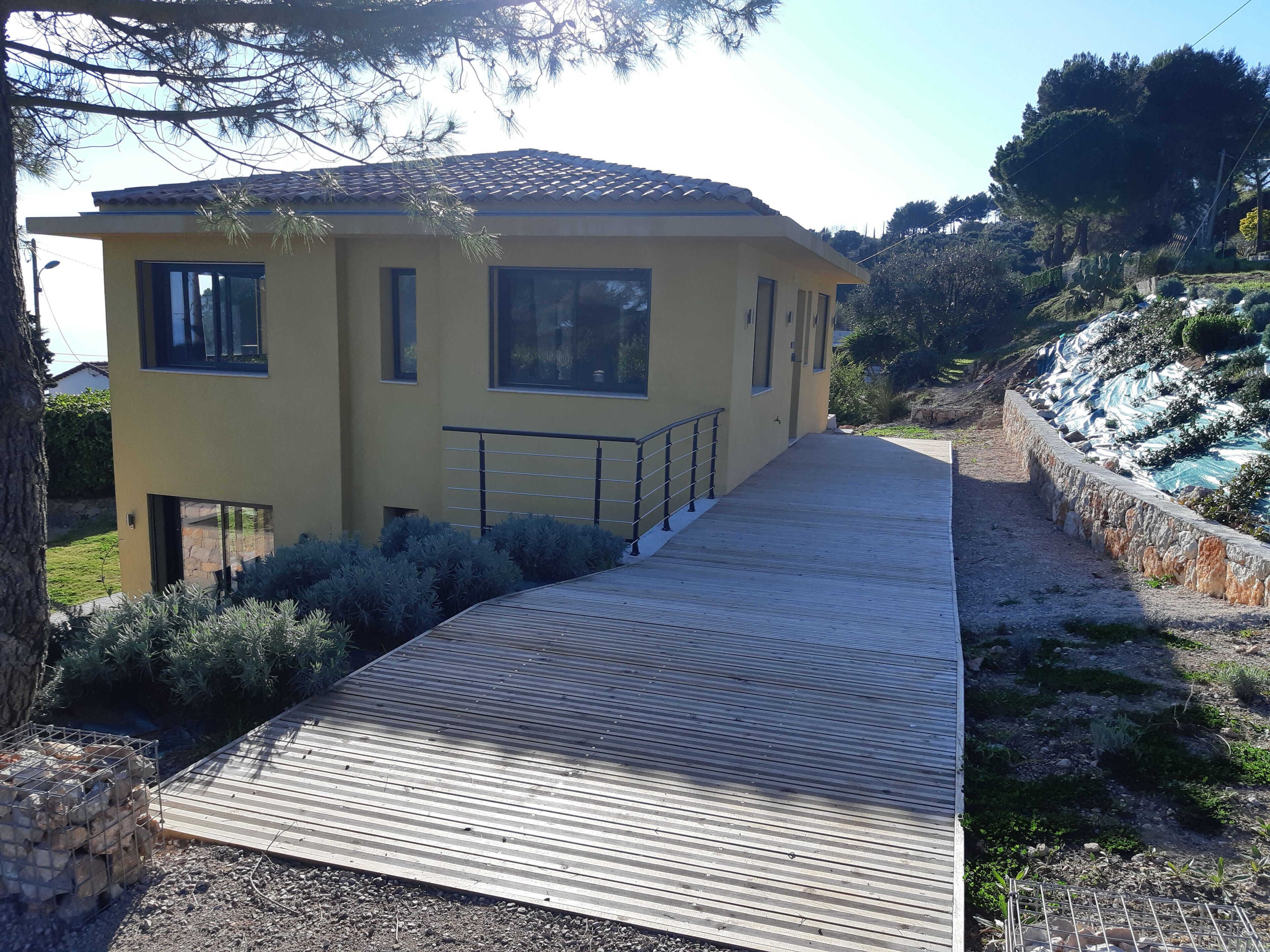 A yellow building with a tiled roof, a wooden deck, and a stone retaining wall.