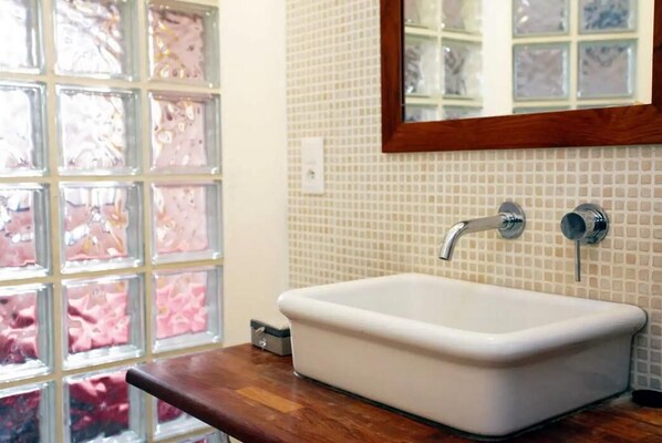 Une salle de bain avec un lavabo blanc, un plan de travail en bois et un mur recouvert de carreaux.