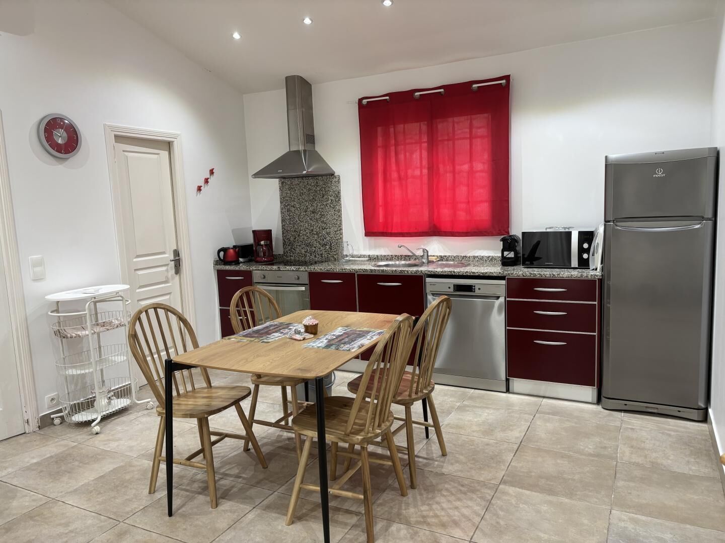 A compact kitchen with a dining area, equipped with a stainless steel refrigerator, a coffee maker, and a dishwasher.