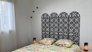 Un dormitorio con colcha estampada, cabecero decorativo, lámparas de noche y una ventana con cortinas.