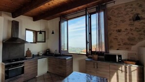 A modern kitchen with wooden cabinets, a stove, and a large window offering a view of the countryside. - La Maison du Chateau (SAINT-JEANNET)