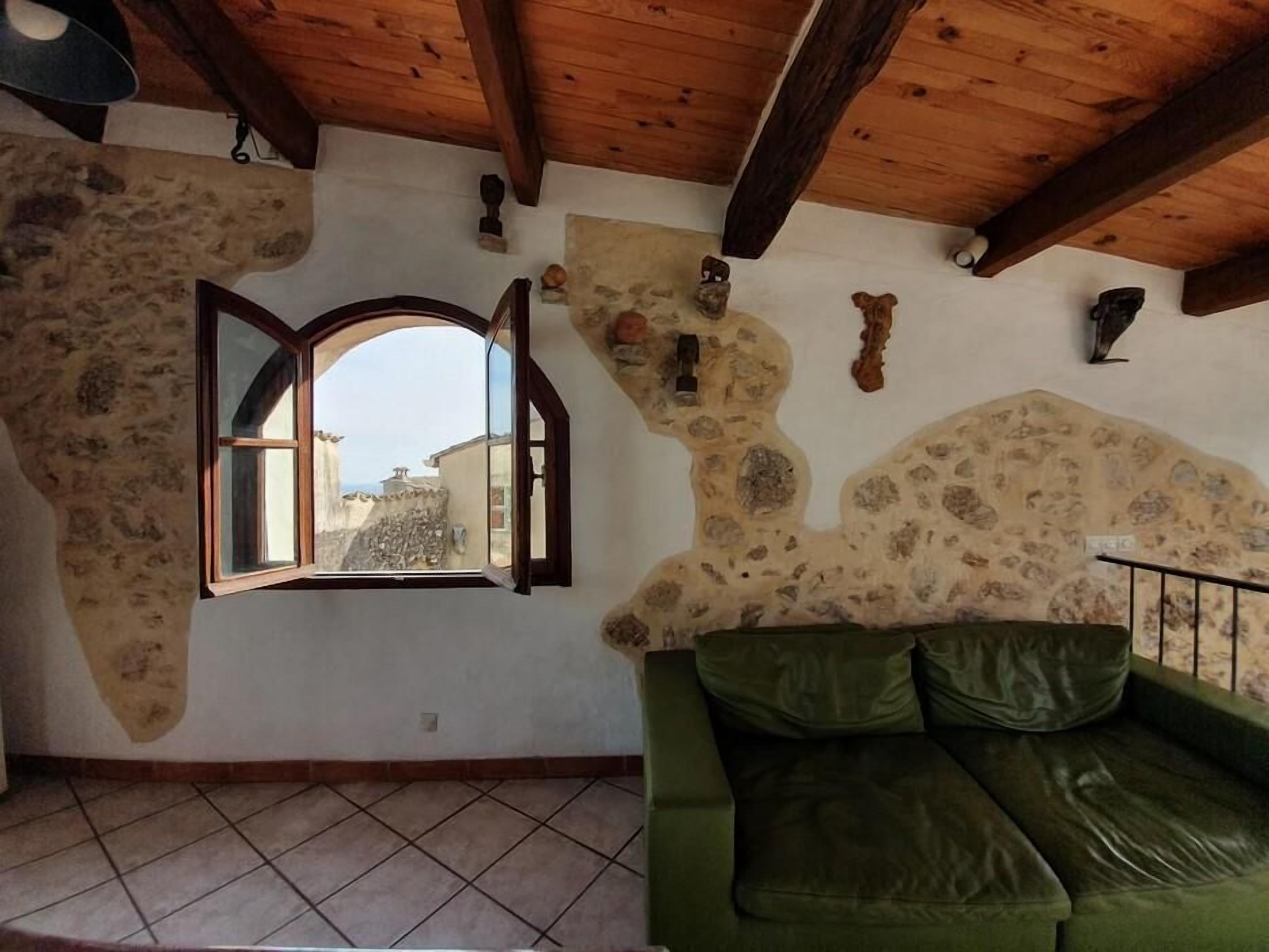 A room with a stone wall, a green leather sofa, a wooden ceiling, and a window with an open shutter.
