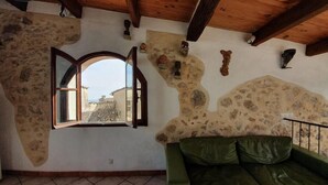 A room with a stone wall, a green leather sofa, a wooden ceiling, and a window with an open shutter. - La Maison du Chateau (SAINT-JEANNET)