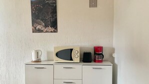 A kitchenette with a microwave, coffee maker, and kettle on a white cabinet. A picture of a mountainous landscape hangs on the wall.