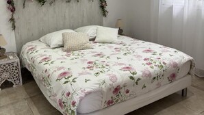 A bedroom with a floral bedspread, a wooden headboard, and a window with sheer curtains.