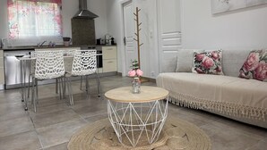 A modern living room with a round wooden coffee table, a sofa with floral cushions, and a kitchen area with a gas stove and white cabinets.