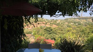 An outdoor patio with a glass table and wicker chairs, overlooking a scenic landscape with houses and greenery.