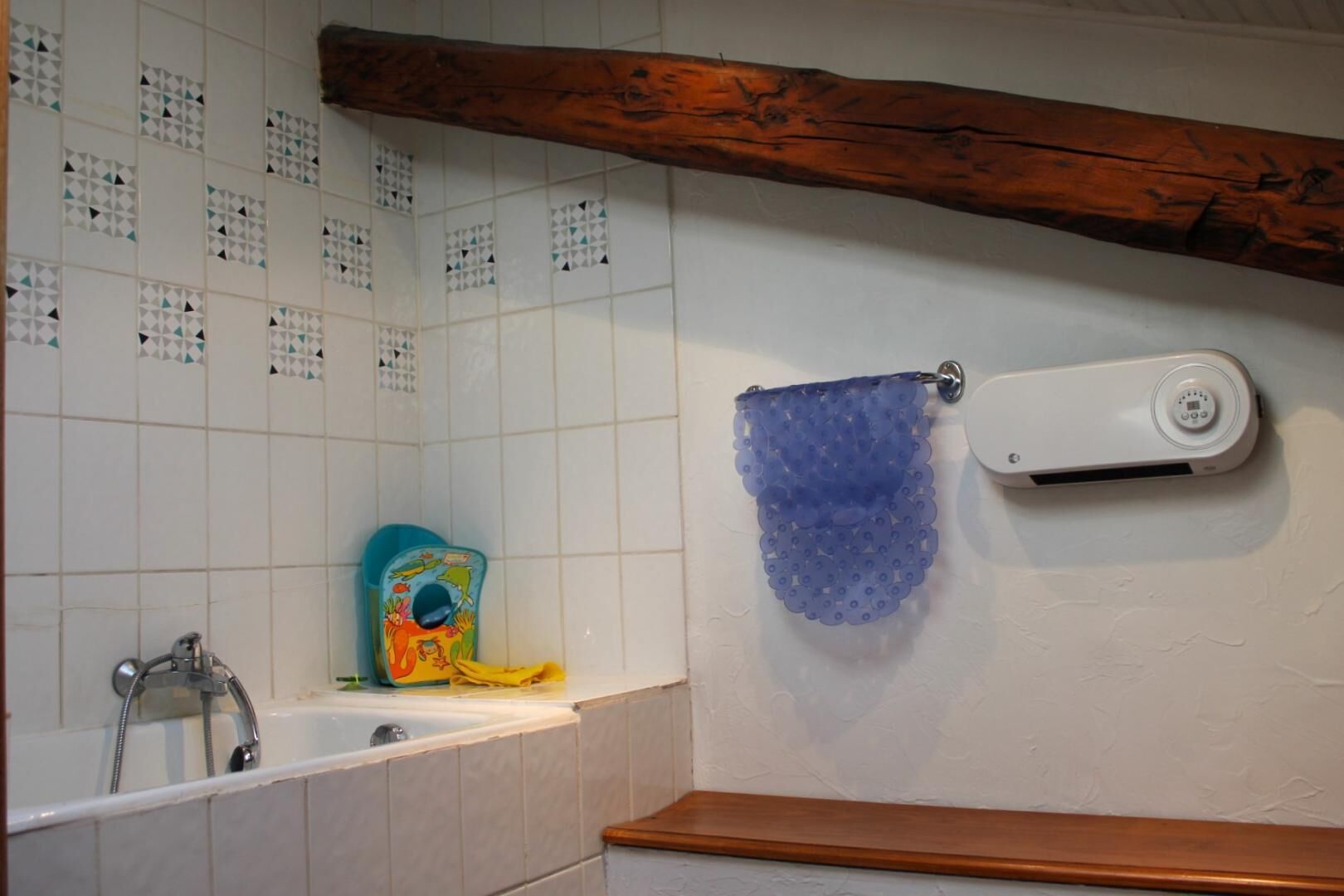 Een badkamer met een bad, een douche, een handdoekrek met een blauwe handdoek en een badspeelgoed voor kinderen.