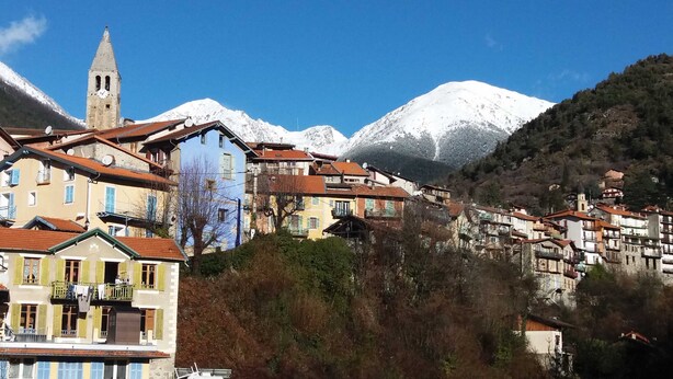 A mountainous village with traditional buildings, a church tower, and snow-capped peaks in the background.