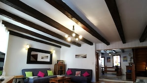 A cozy living room with a dark blue sofa, wooden coffee table, and exposed wooden beams on the ceiling.