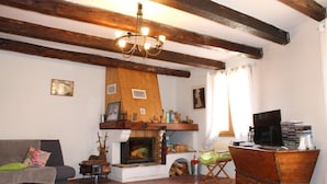 A cozy living room with a fireplace, wooden beams, a sofa, a coffee table, and a TV.