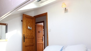A bedroom with a bed, a wooden wardrobe, a wall-mounted lamp, and a skylight.