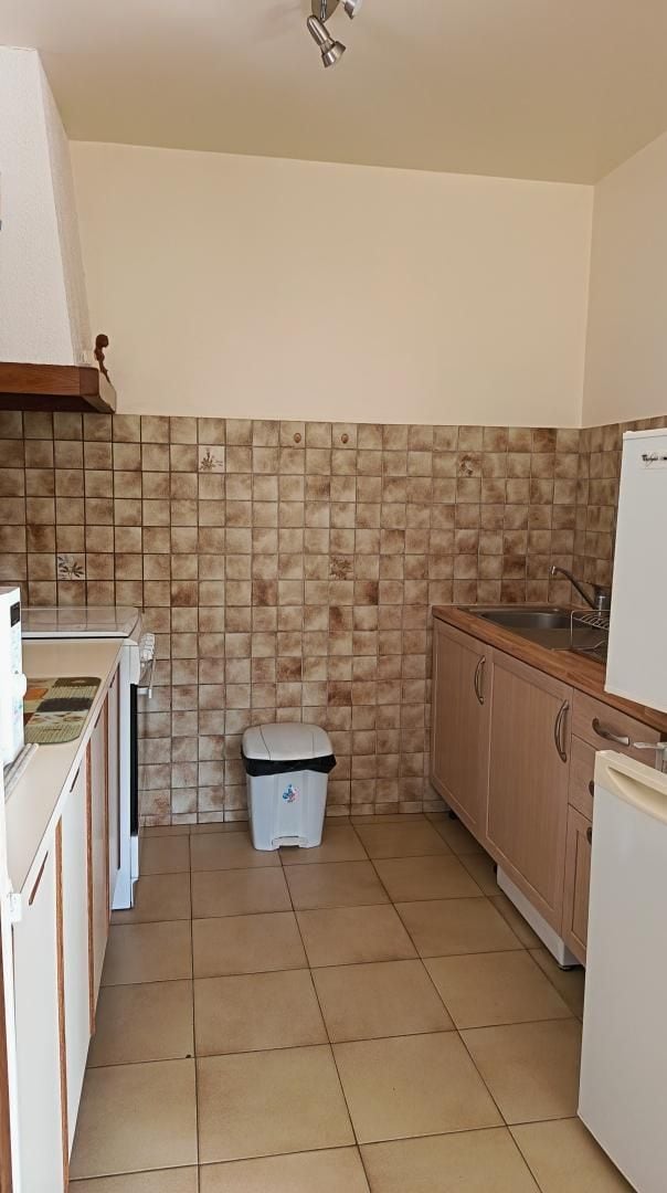 A compact kitchen with a tiled backsplash, a sink, and a trash bin.