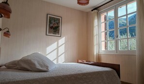 A bedroom with a bed, a window with a view of mountains, a framed picture on the wall, and a hanging light fixture. - Ascent from St. Jean d'Ermi to BREIL-SUR-ROYA (BREIL-SUR-ROYA)