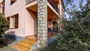 A two-story building with a stone column, a balcony with a metal railing, and a staircase leading to the entrance. - Ascent from St. Jean d'Ermi to BREIL-SUR-ROYA (BREIL-SUR-ROYA)
