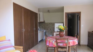 A dining area with a table set for two, a kitchen in the background, and a wardrobe to the left. - Montée St Jean d'Ermi - BREIL-SUR-ROYA (BREIL-SUR-ROYA)