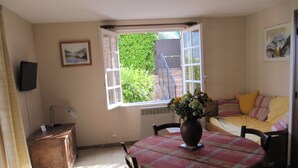 A room with a dining table, chairs, a sofa, a window with an open shutter, and a wall-mounted speaker. - Montée St Jean d'Ermi - BREIL-SUR-ROYA (BREIL-SUR-ROYA)