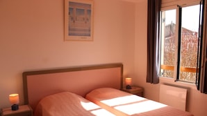 A bedroom with two beds, a nightstand with a lamp, a framed picture on the wall, and a window with curtains.