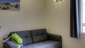 A grey sofa with a green plush toy, a wall-mounted light fixture, and a window with curtains.