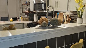 A modern kitchen with white cabinets, a stainless steel microwave, a sink with a large island, and two yellow bar stools.