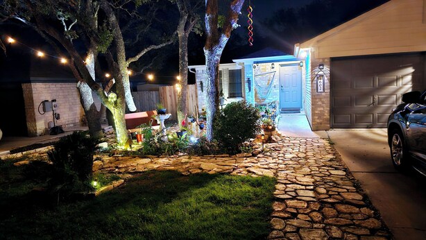A residential driveway with a stone pathway leading to a garage. There are decorative lights and plants along the pathway.