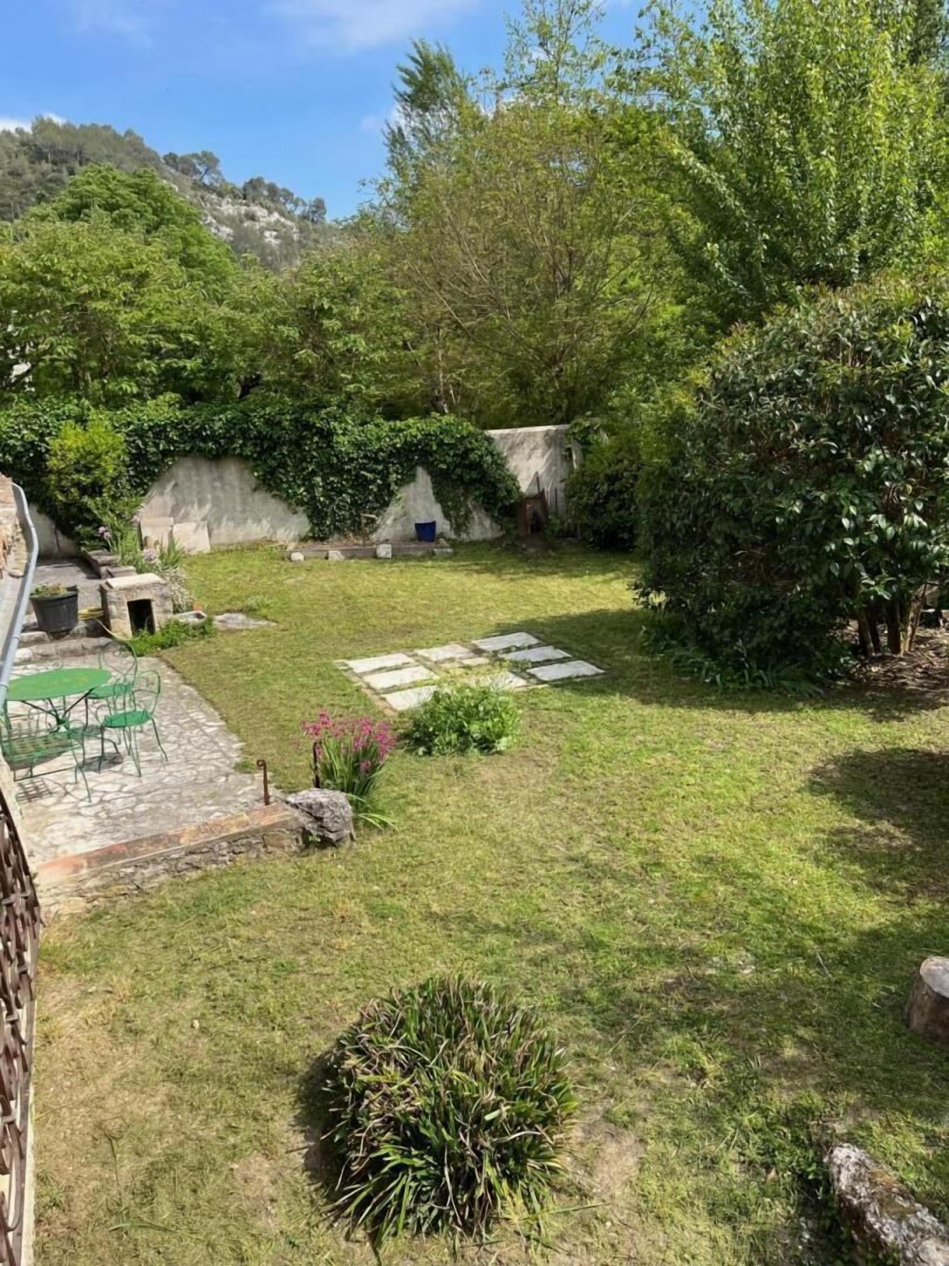 Un jardin avec une terrasse en pierre, une petite table et des chaises.