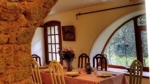 A dining area with a stone wall, wooden chairs, a table with a floral centerpiece, and a window with a view of greenery.