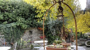 A garden with a stone fountain, potted plants, and metal chairs.